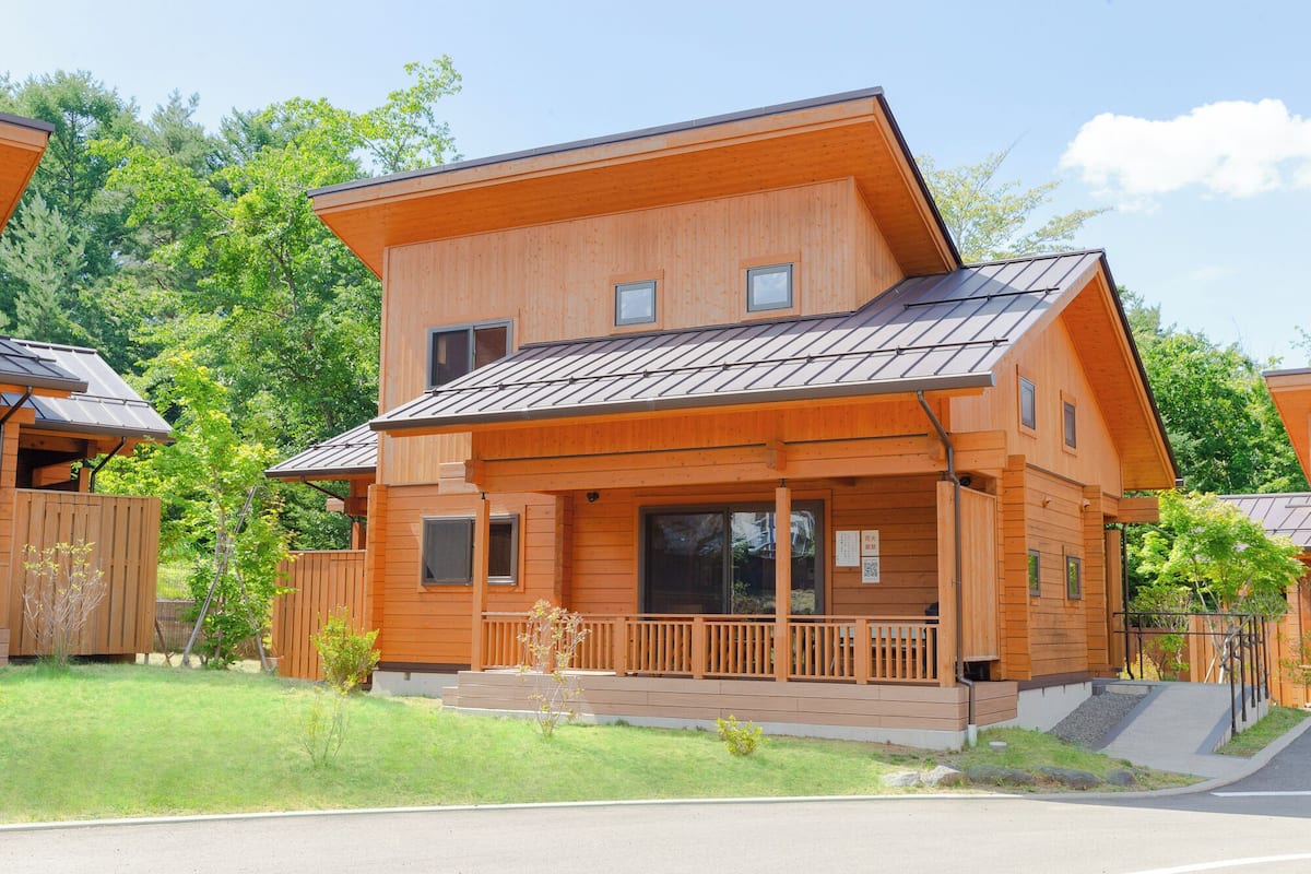 A two-story wooden cabin with a balcony, large windows, and a sloped roof.