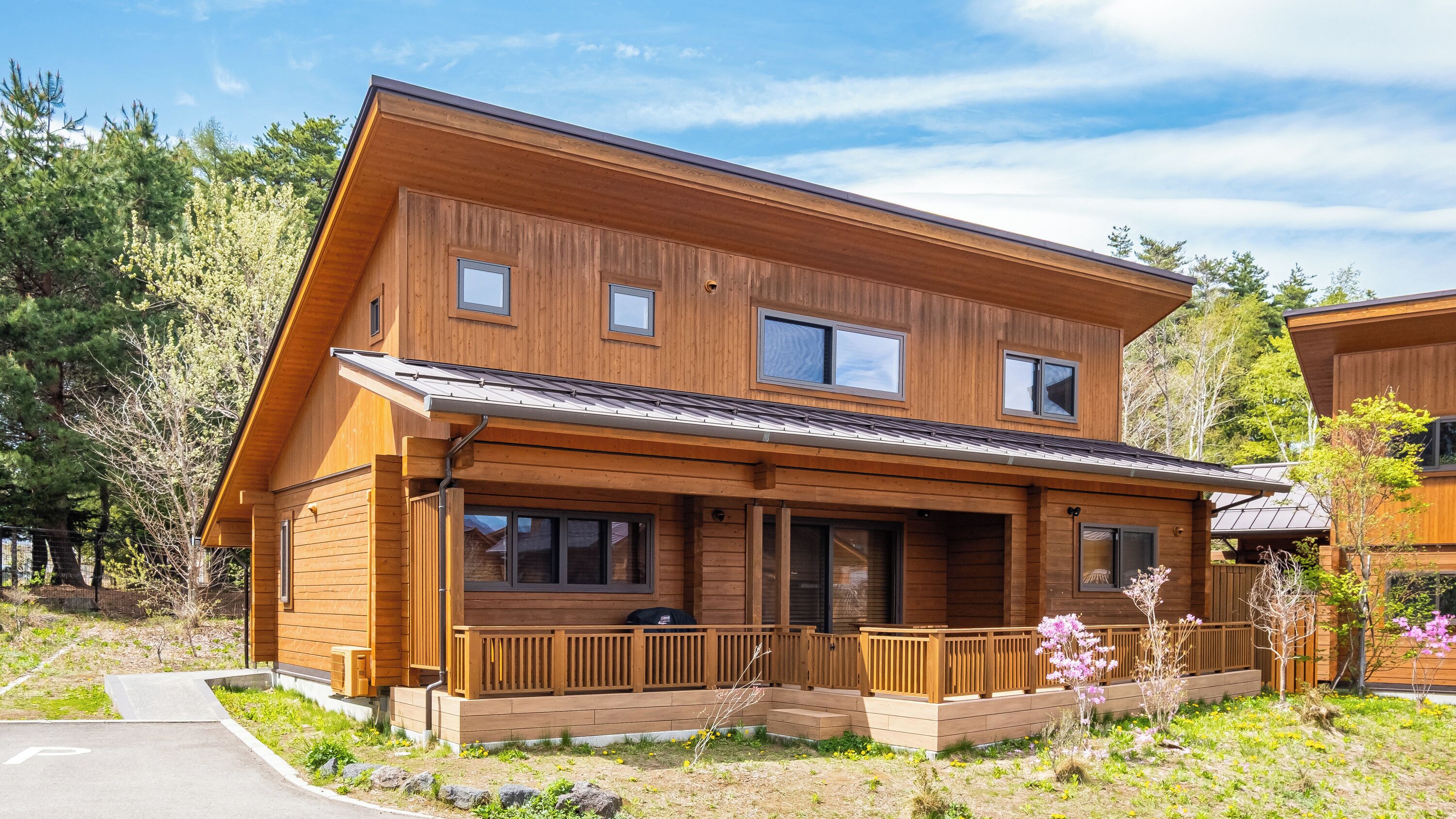 A two-story wooden cabin with a porch, large windows, and a sloped roof.