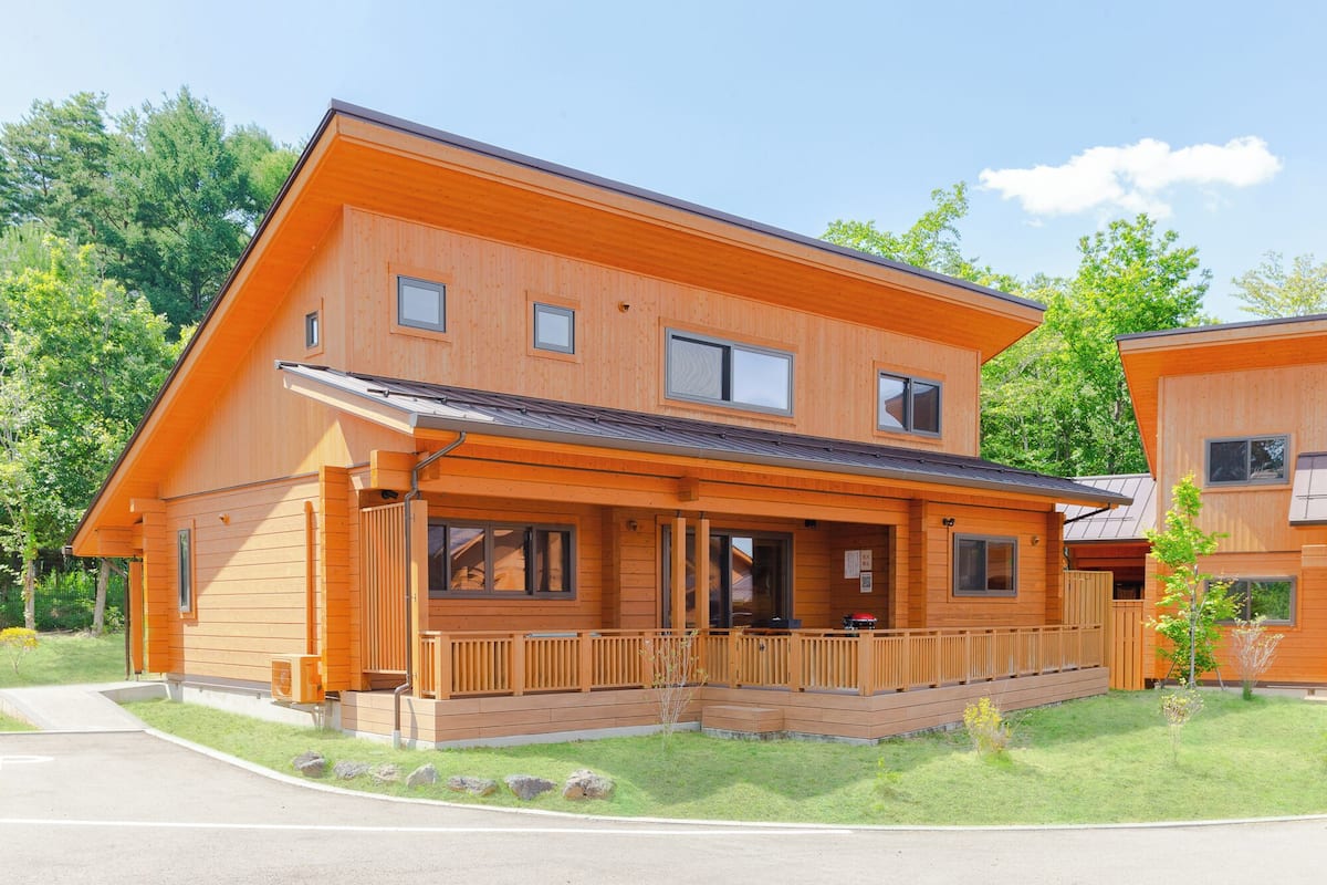 A two-story wooden house with a covered porch, a garage, and a small garden.