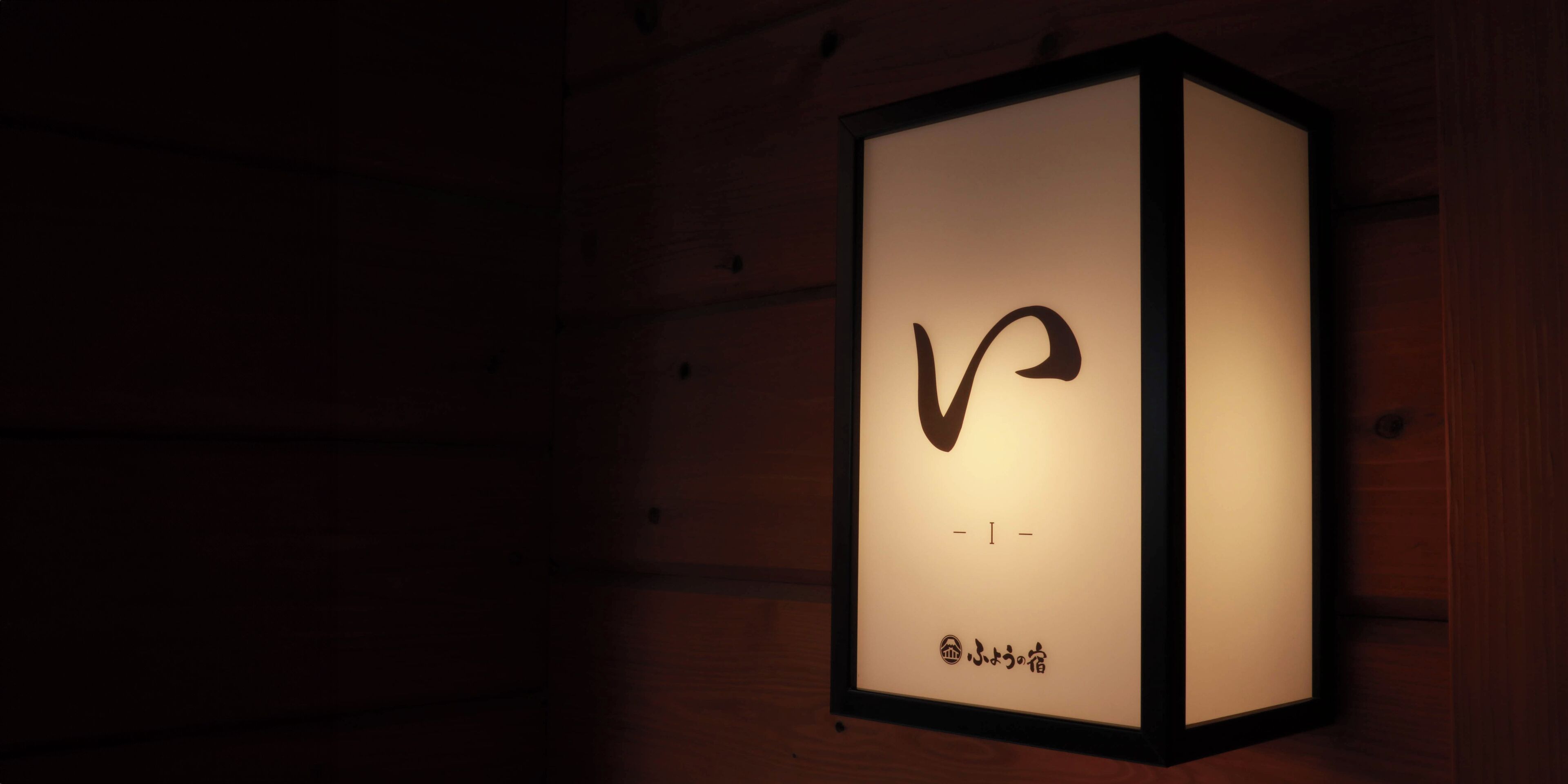 Een wandlamp in een lijst, met een gestileerd ontwerp, mogelijk een logo, en tekst eronder.