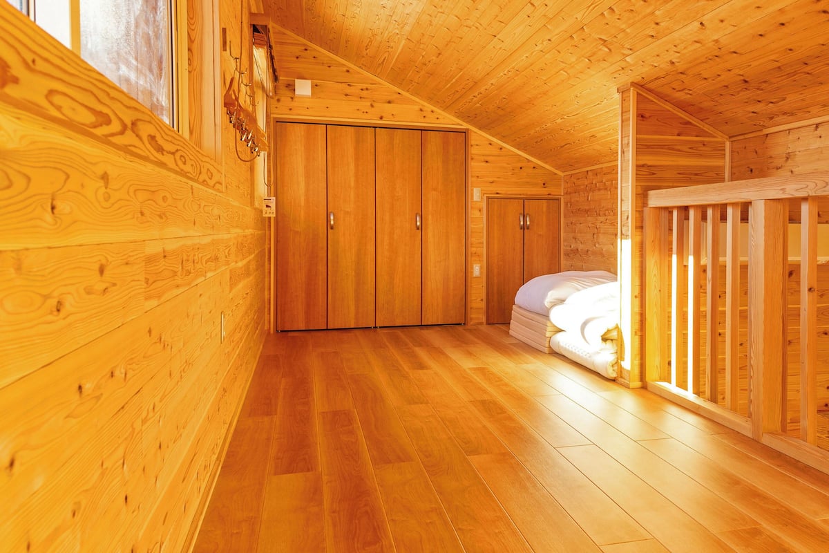 A wooden cabin interior with a bedroom featuring a bed, a wooden wardrobe, and a crib.