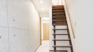 Un pasillo estrecho con suelo de baldosas, una escalera de madera y un muro enlosado.