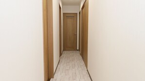 Un pasillo estrecho con puertas de madera a ambos lados y suelo de color claro.