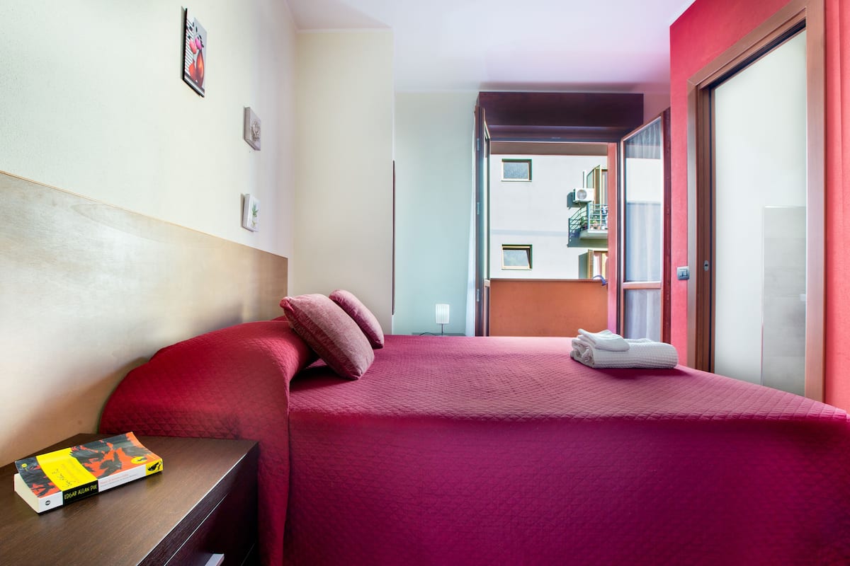 Habitación de hotel con cama, mesita de noche y vistas al balcón exterior.
