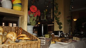 A buffet table with various breads, pastries, and a vase of red flowers. - Behringers Freizeit- & Tagungshotel (Goessweinstein)