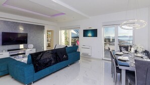 En moderne stue med sofa, fjernsyn og spiseområde med et bord dækket til to.