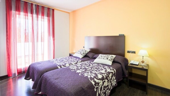 A hotel room with two beds, a nightstand with a lamp, and a window with red curtains. - Hotel La Duquesa (Pinos Genil)
