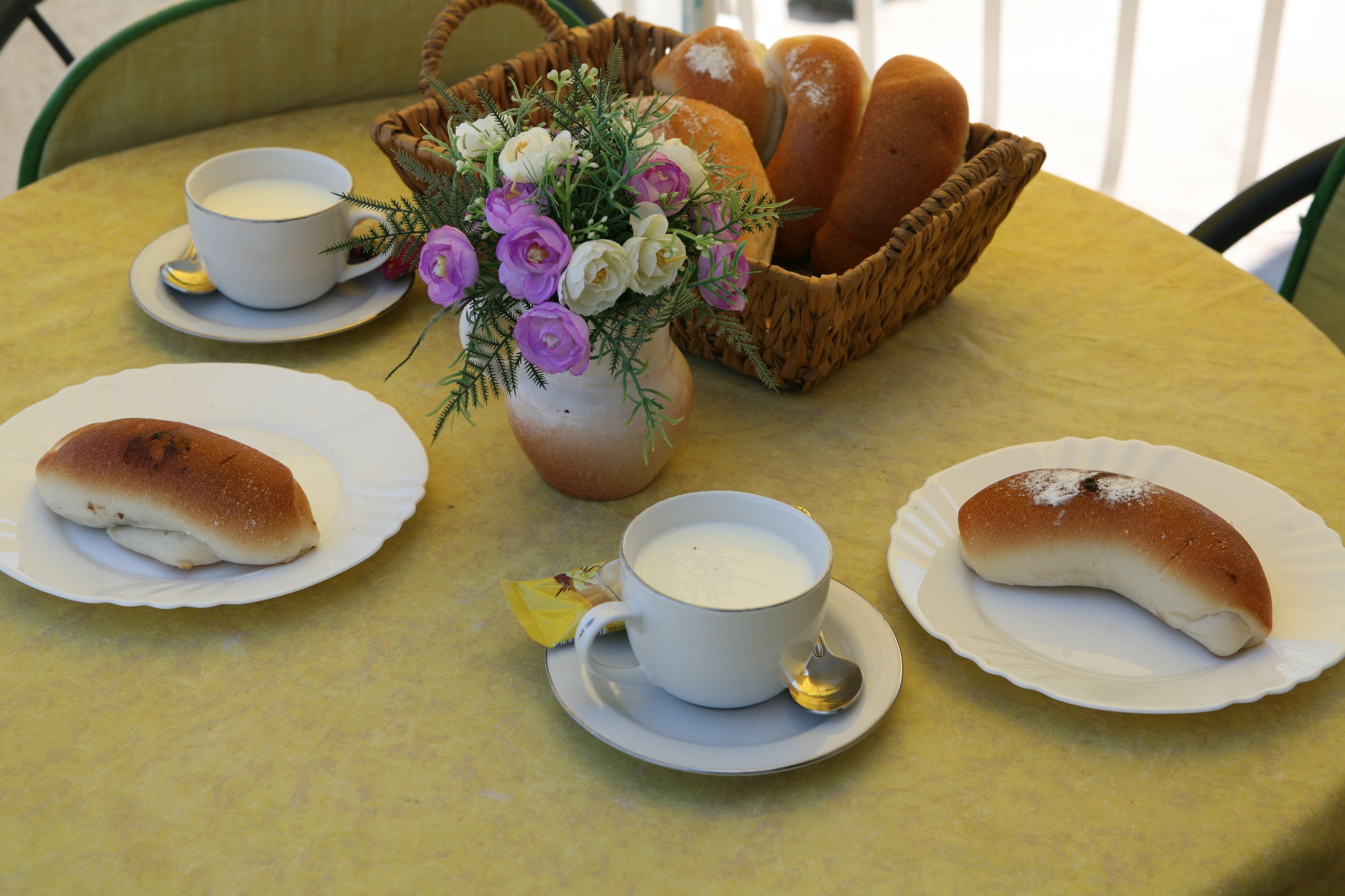 A table with a basket of bread, a vase of flowers, and two cups of coffee.