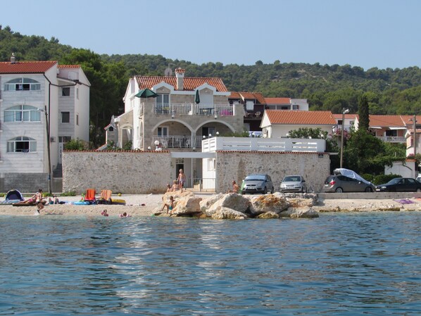 A coastal building with a stone facade, multiple balconies, and a tiled roof.