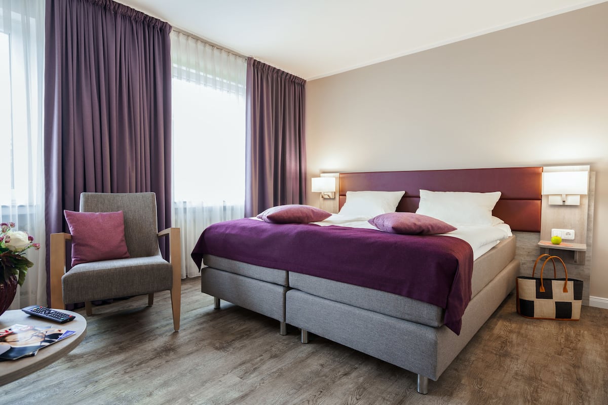 Une chambre d’hôtel moderne avec un grand lit, une chaise, une petite table et une table de chevet avec une lampe.