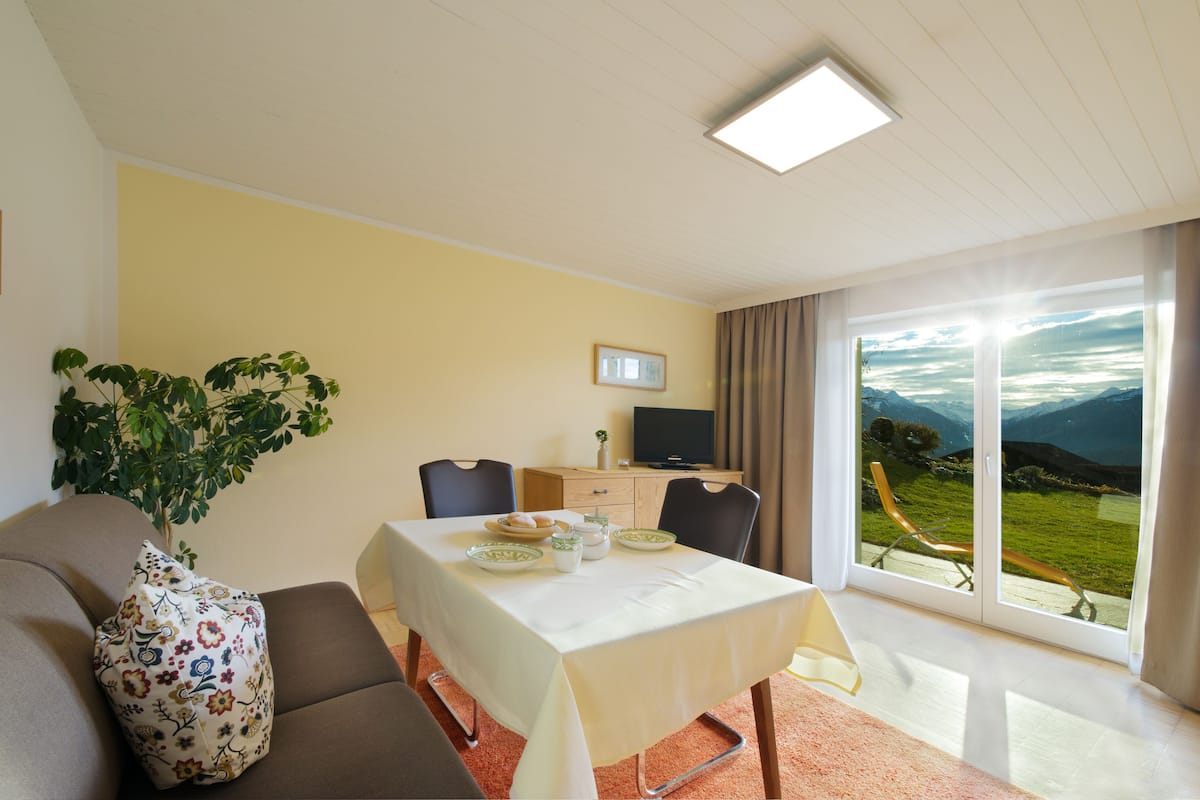 Una habitación con una mesa de comedor, sillas, un sofá, un televisor y un ventanal con vistas al exterior.