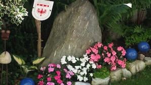 Un jardín con una roca grande, flores rosadas y blancas, y decoraciones esféricas azules.