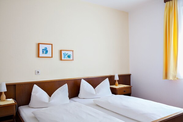 A hotel room with two beds, a nightstand with a lamp, and two framed artworks on the wall. - Tiroler Alpenhof (Patsch)