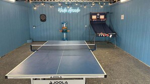 A ping pong table with a neon sign reading 'Wave Arcade,' a dartboard, and a small play area with a slide.
