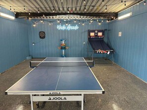 A ping pong table with a neon sign reading 'Wave Arcade,' a dartboard, and a small play area with a slide.