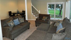 A living room with two sofas, a dining table, and a staircase leading to a balcony.
