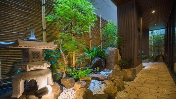 A traditional Japanese garden with a stone lantern, rocks, and a bamboo fence. - Hotel Yu-shu (Osaka)