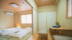 A traditional Japanese room with tatami flooring, a futon bed, a wooden table, and a sliding door closet. - Hotel Yu-shu (Osaka)