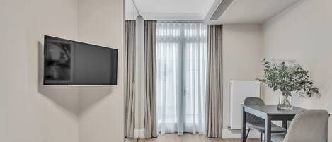 A modern hotel room with a flat-screen TV mounted on the wall, a dining table with chairs, and a potted plant on the table.