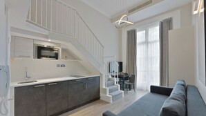 A modern kitchen with a built-in oven and microwave, a staircase leading to a dining area, and a grey sofa in the living space. - Cleveland Residences Paddington (London)