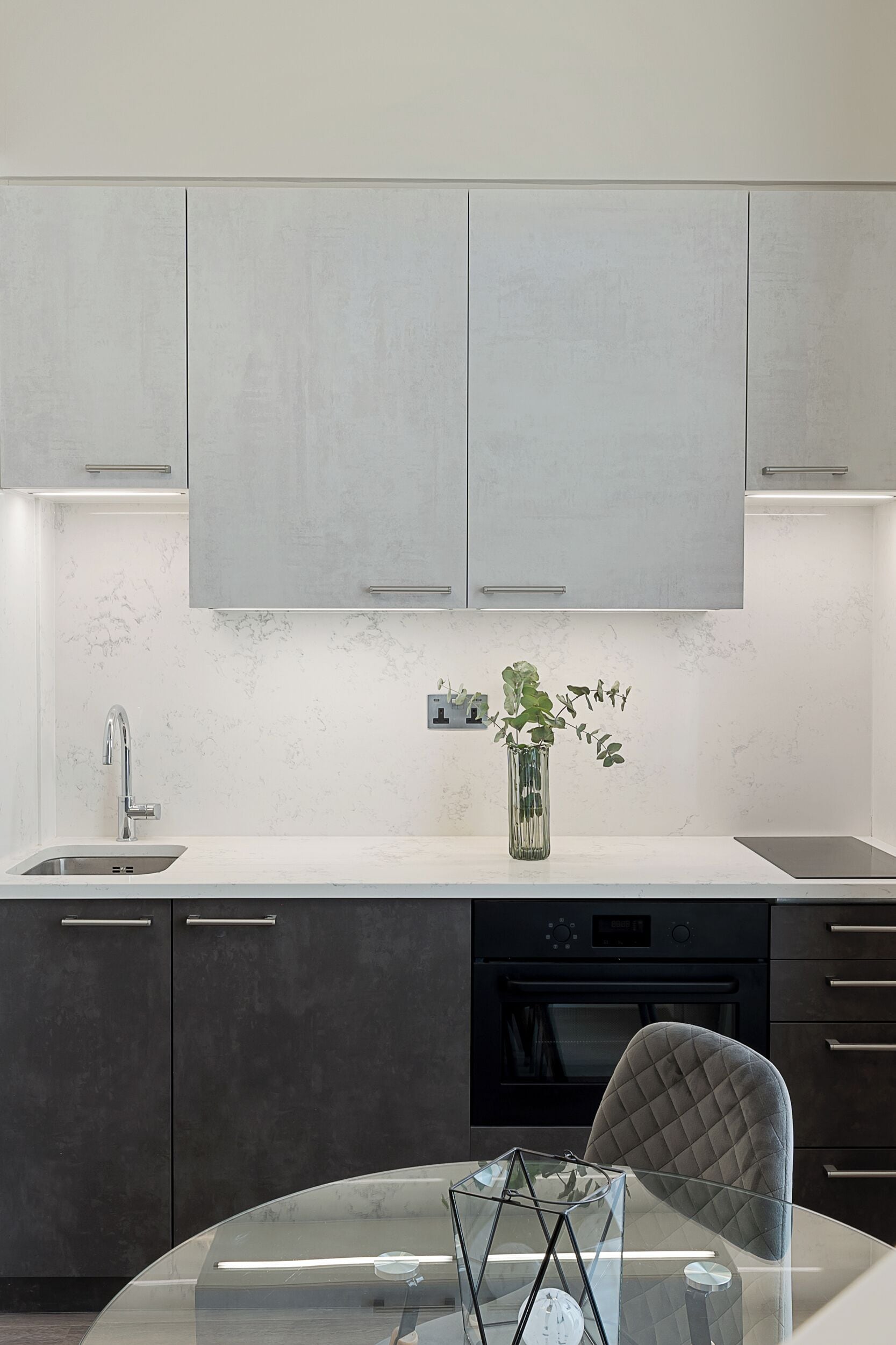 Una cocina moderna con encimera de mármol, una mesa de comedor de vidrio y un horno negro.