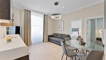 Un salón moderno con una mesa de comedor de cristal, sofá gris y un amplio ventanal con cortinas.