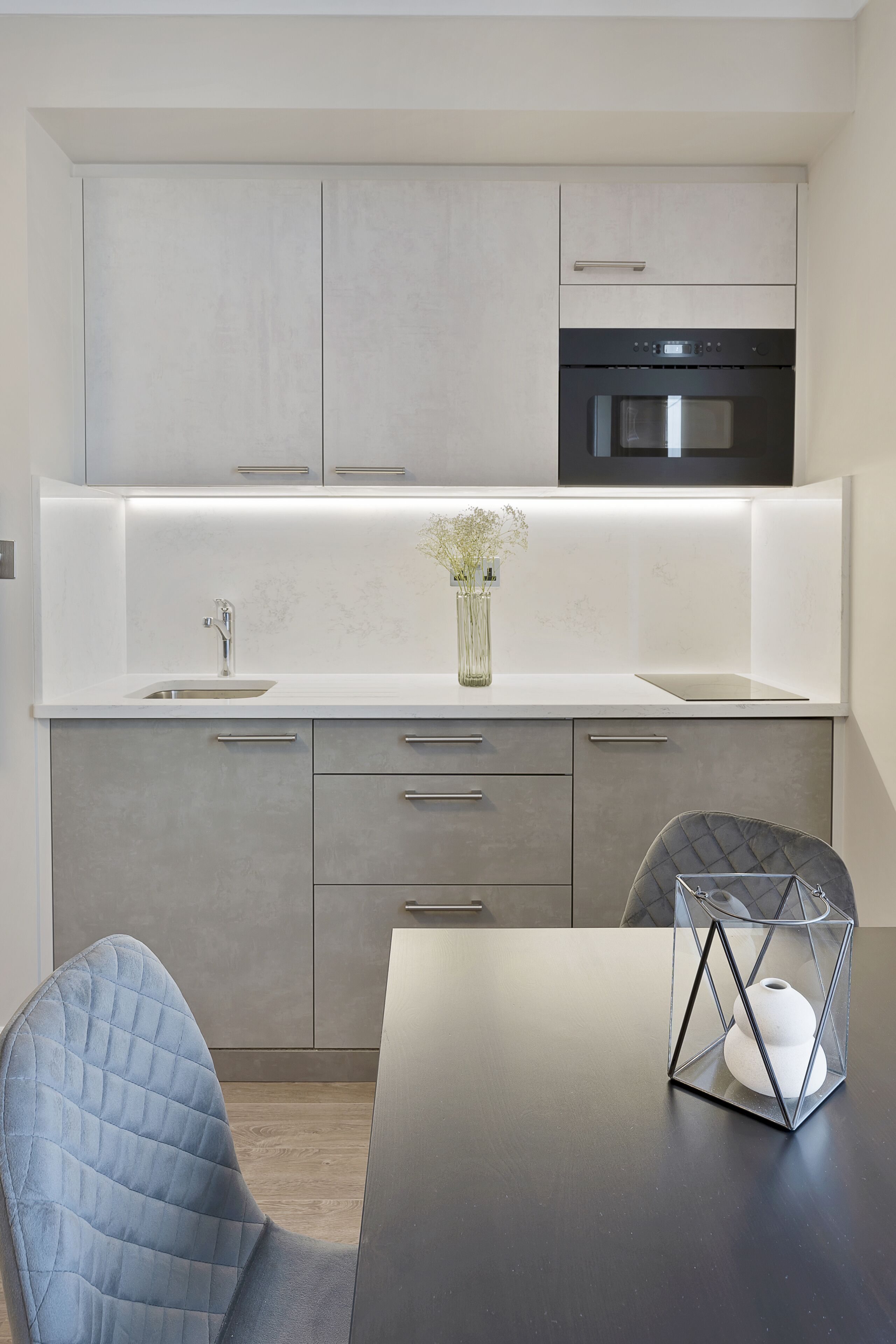 A modern kitchen with a built-in oven, a sink, and a dining area with a table and chairs.