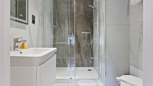 Ein modernes Badezimmer mit einer Duschkabine aus Glas, einem weißen Waschbecken und einem Spiegel.