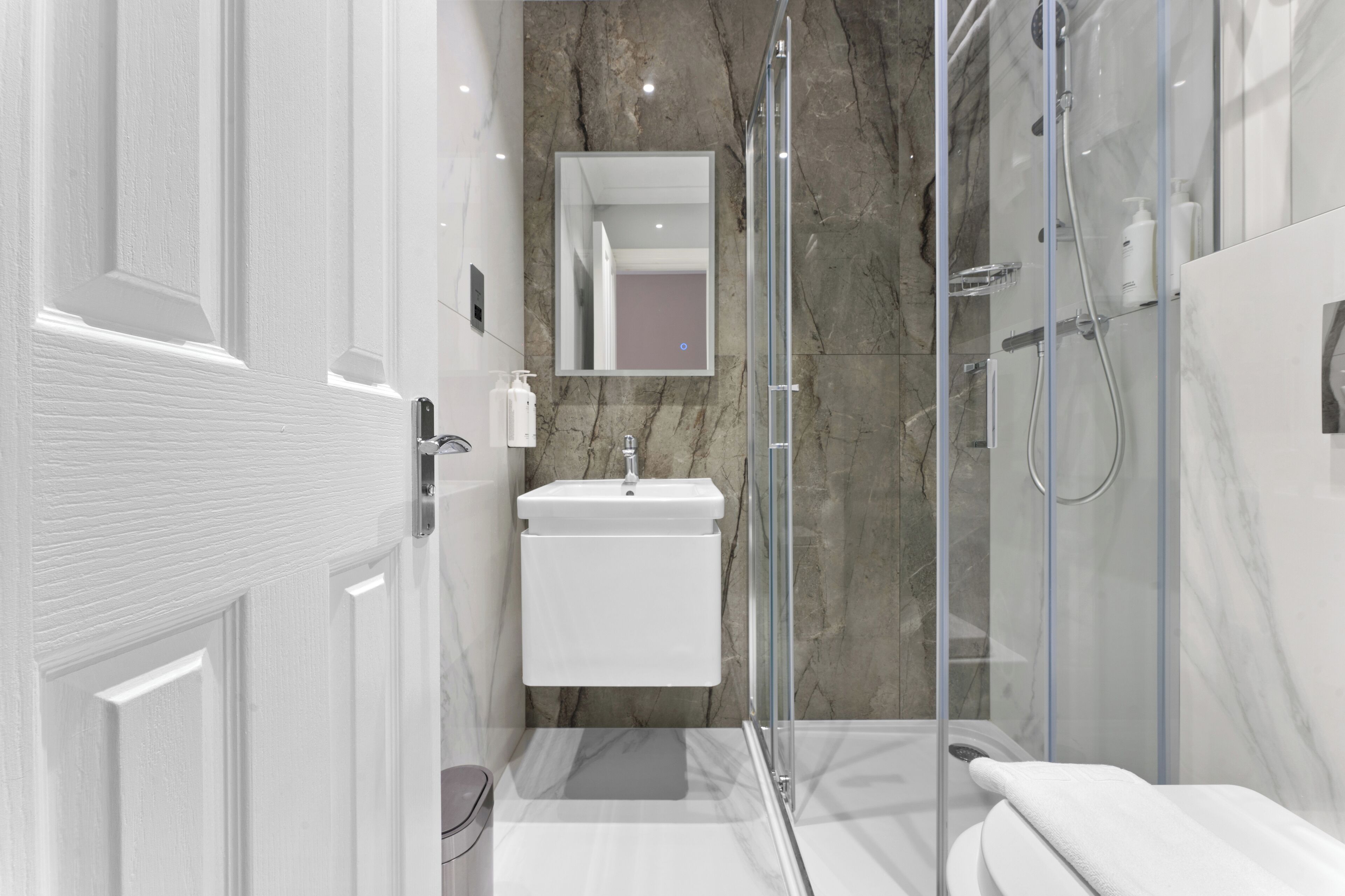 A modern bathroom with a white sink, a glass-enclosed shower, and a marble wall.