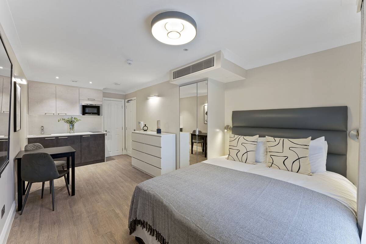 A modern hotel room with a large bed, a desk, and a kitchenette.