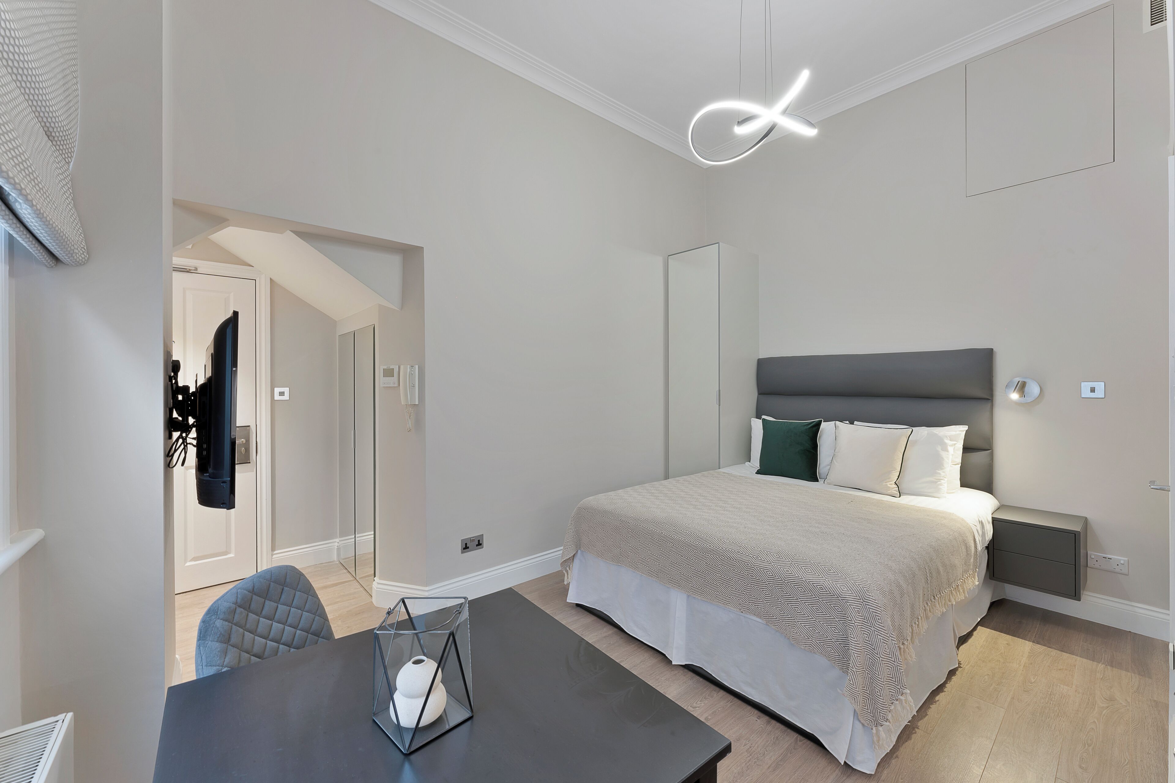 A modern bedroom with a large bed, bedside tables, a desk, and a chair.