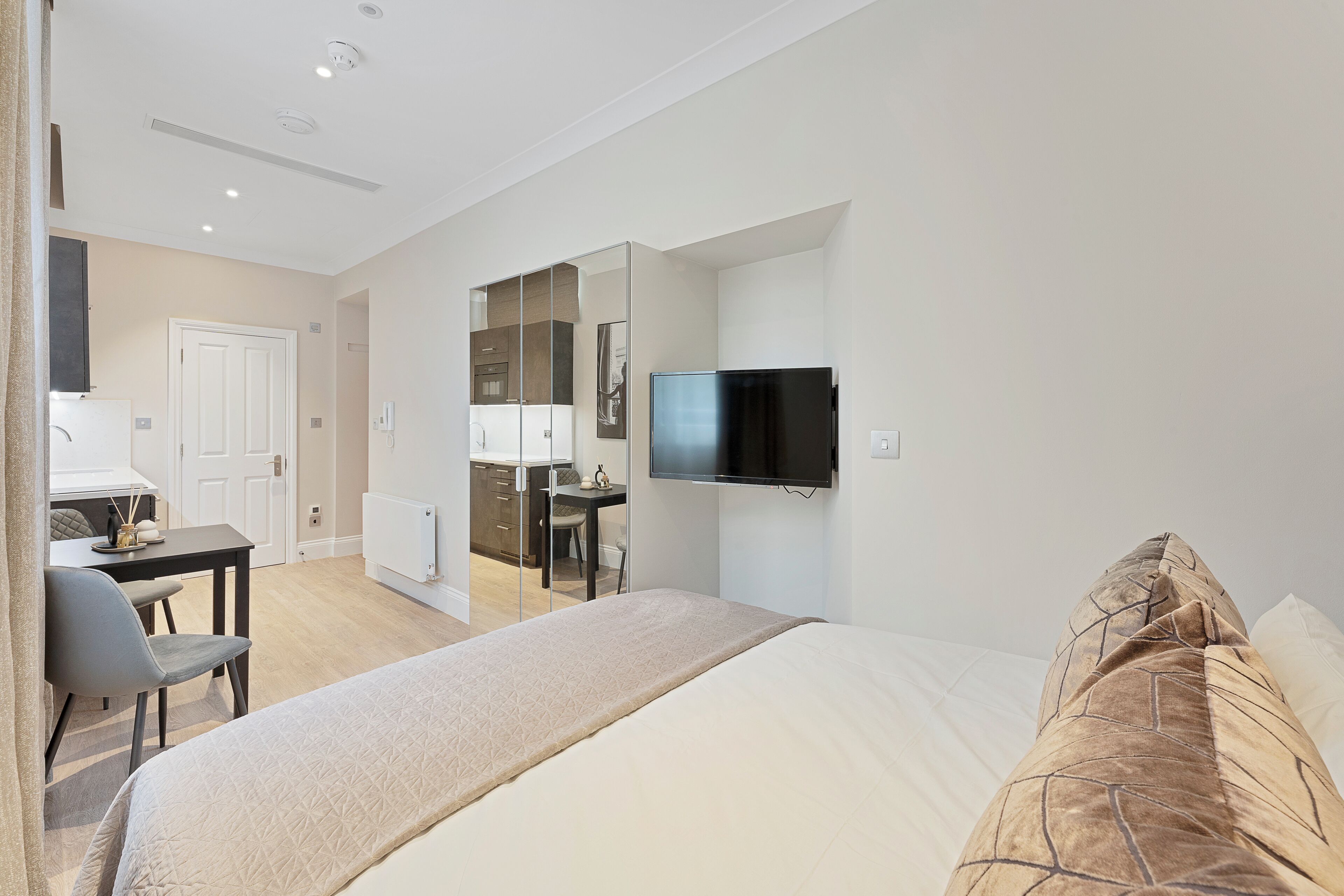 Una habitación de hotel moderna con una cama, un escritorio, una silla, un televisor y un baño visible a través de un separador de vidrio.