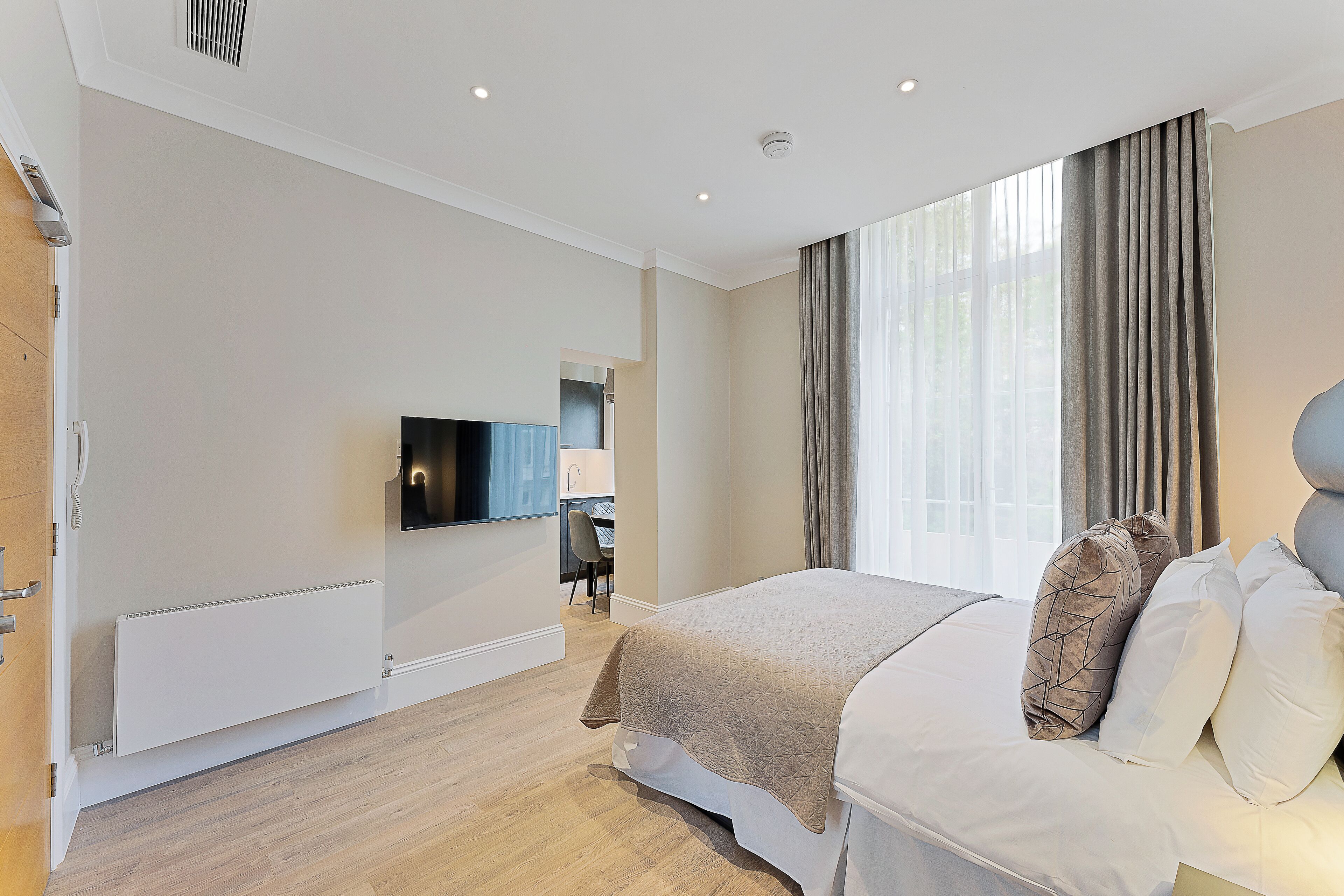 A modern hotel room with a bed, a TV, a desk, and a window with curtains.