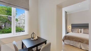 A hotel room with a bed, a table with a vase, and a view of a building and trees outside the window.