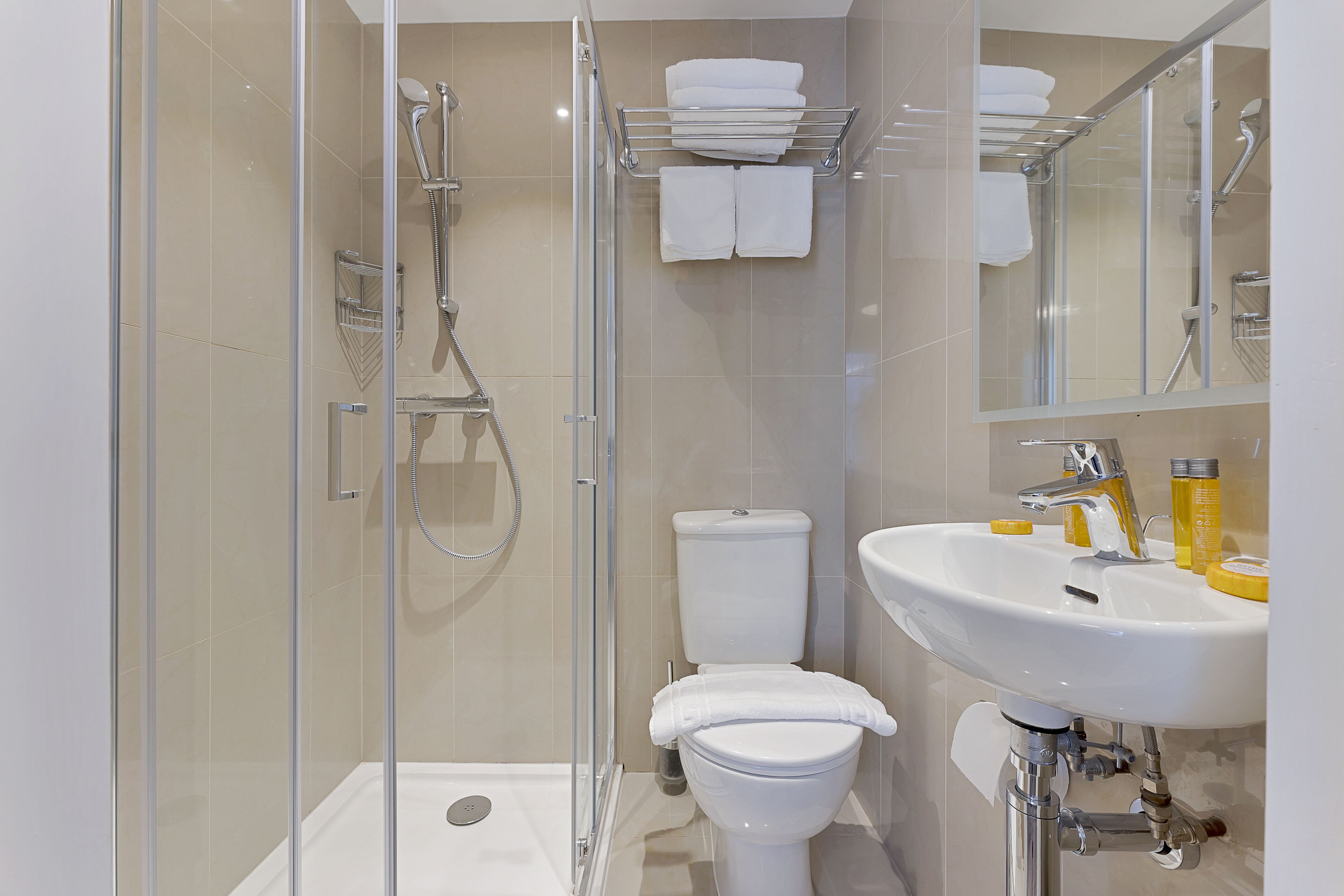 Un baño moderno con cabina de ducha de vidrio, inodoro blanco y lavamanos con artículos de aseo.