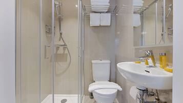 Un baño moderno con cabina de ducha de vidrio, inodoro blanco y lavamanos con artículos de aseo.