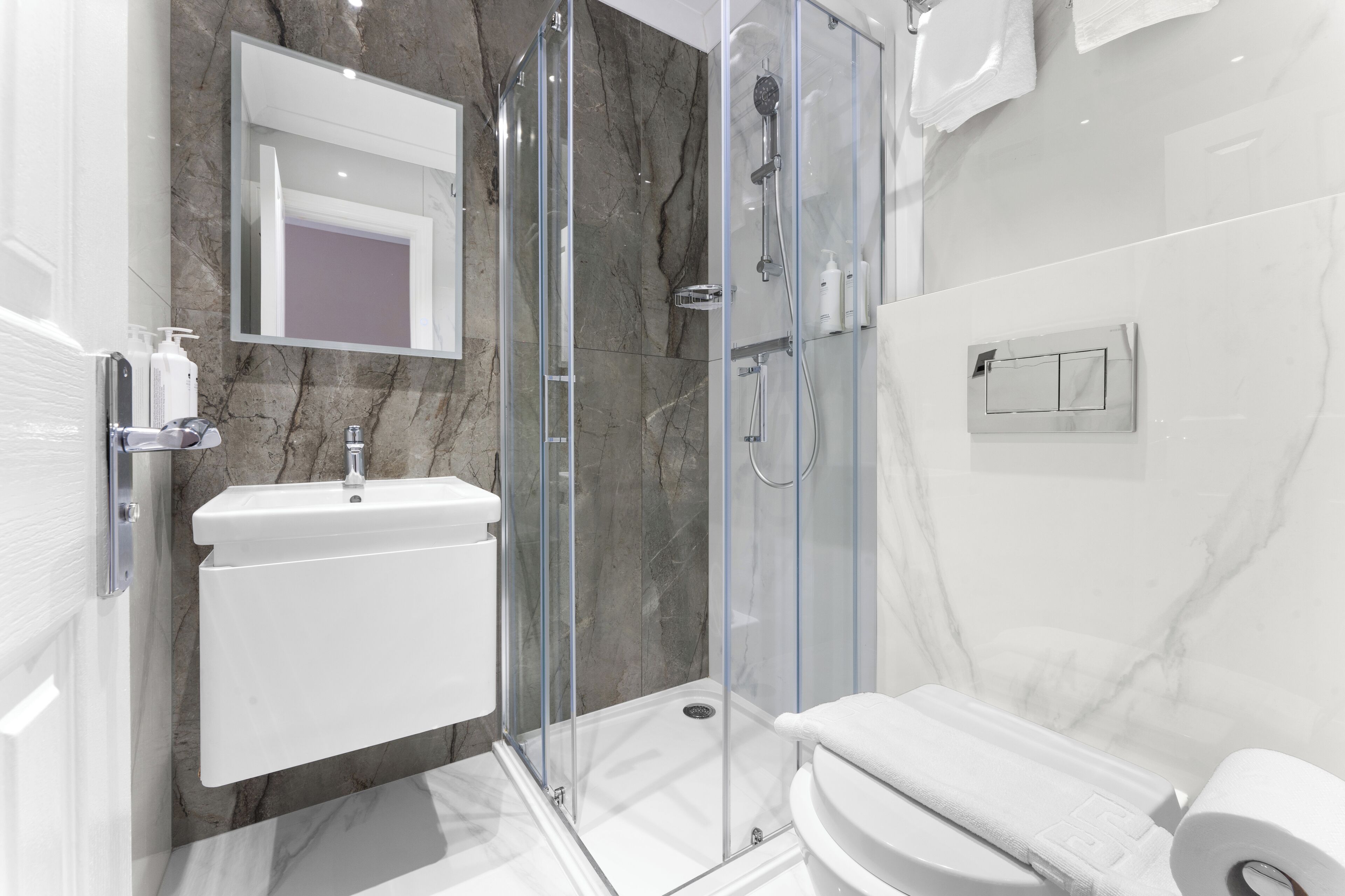 Een moderne badkamer met een douchecabine van glas, een wit wastafeltje en een toilet.