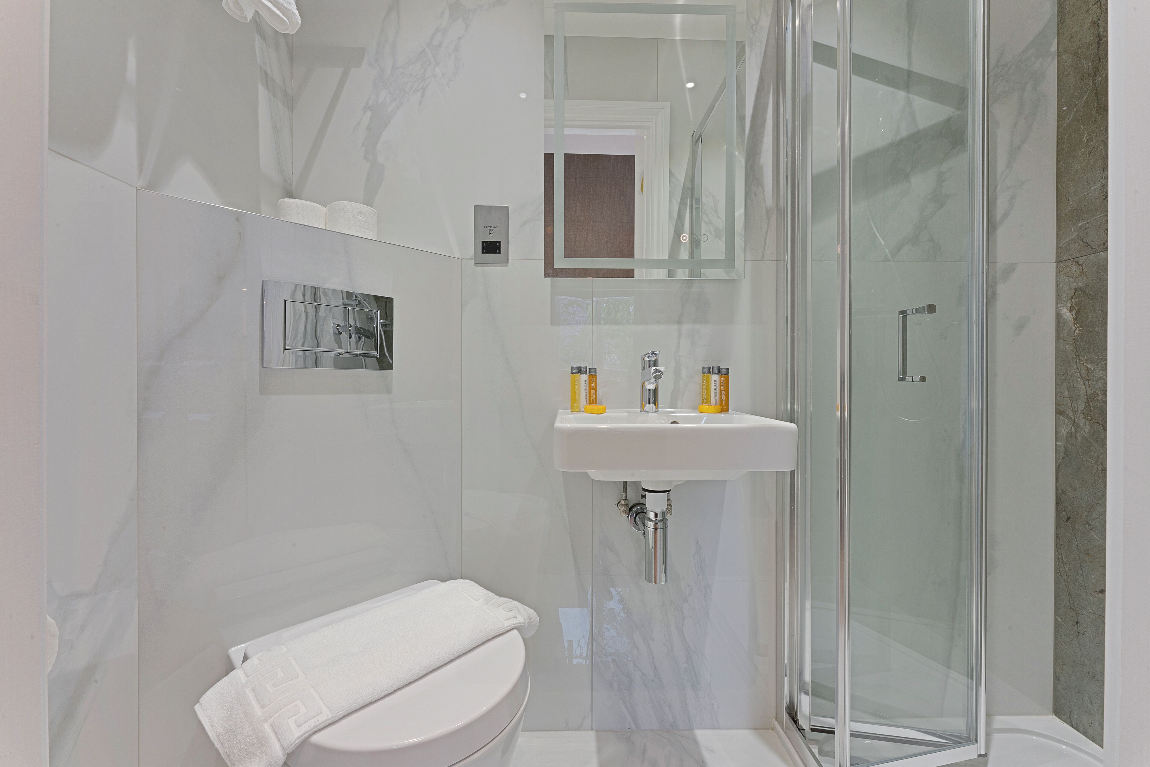 A modern bathroom with a glass shower enclosure, a white toilet, and a sink with yellow soap dispensers.