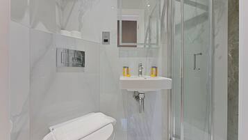 A modern bathroom with a glass shower enclosure, a white toilet, and a sink with yellow soap dispensers.