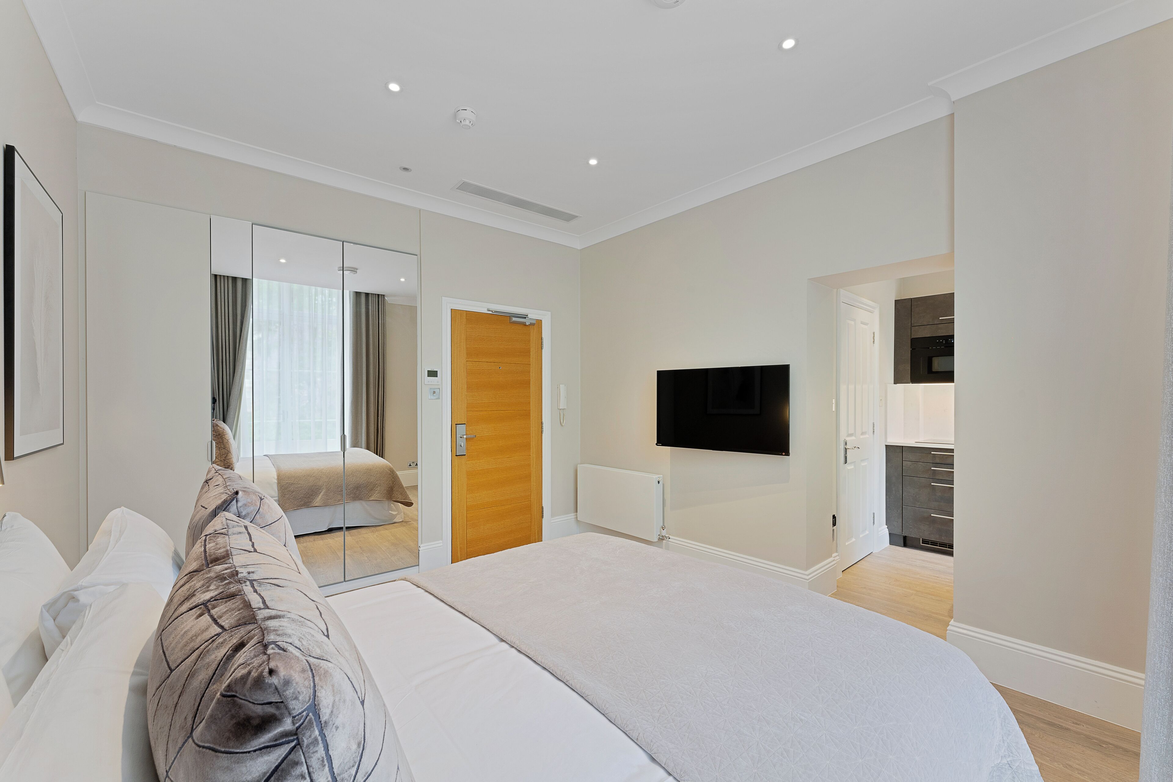 Un dormitorio moderno con una cama grande, un televisor en la pared y una puerta corredera que da al baño.