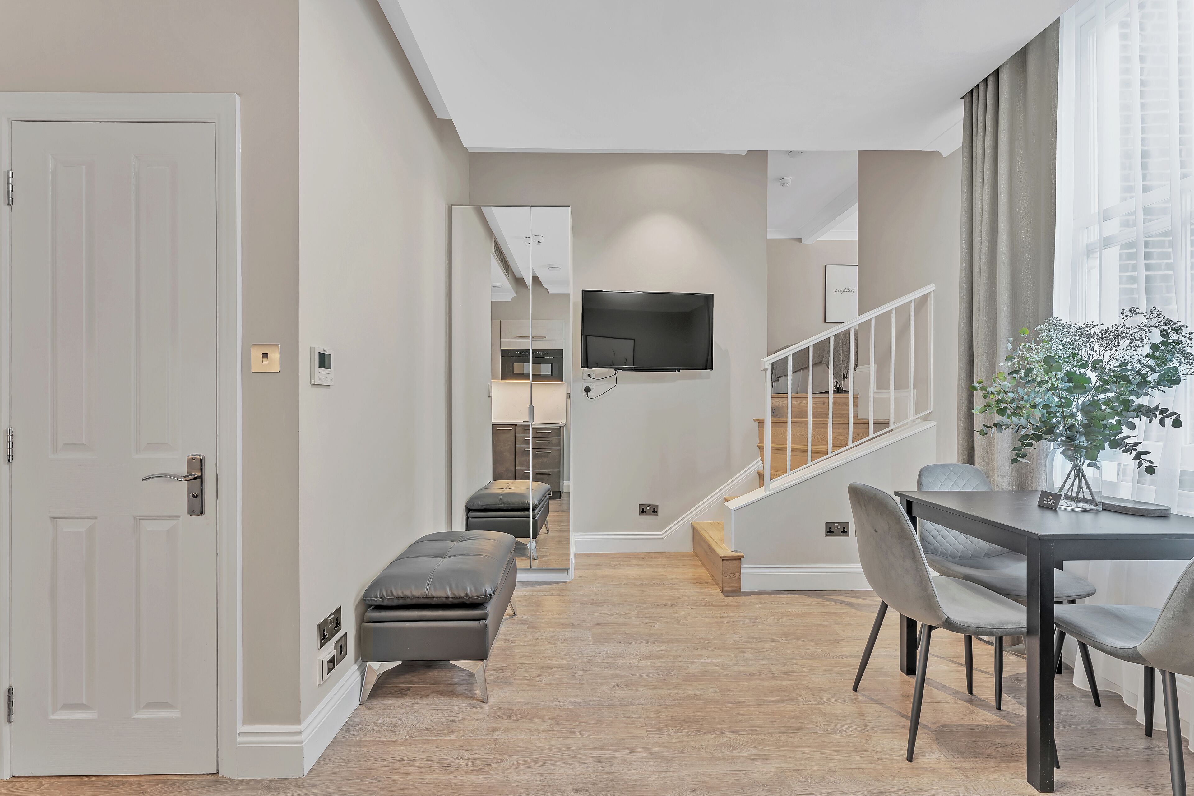 A modern living room with a dining area, a bench, and a staircase leading to another level.