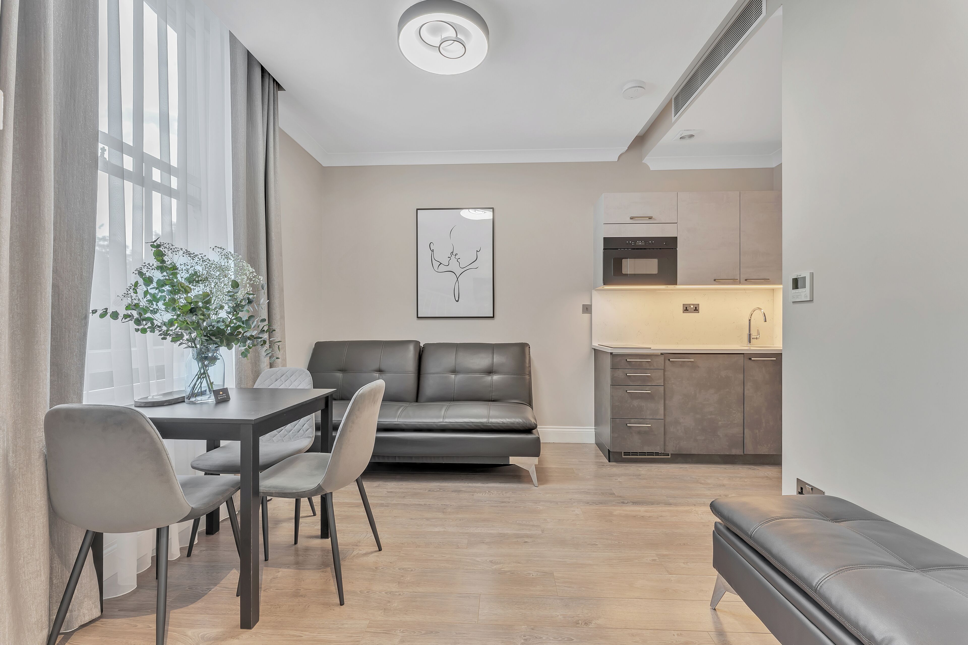 A modern living room with a dining area, a grey sofa, and a kitchen in the background.