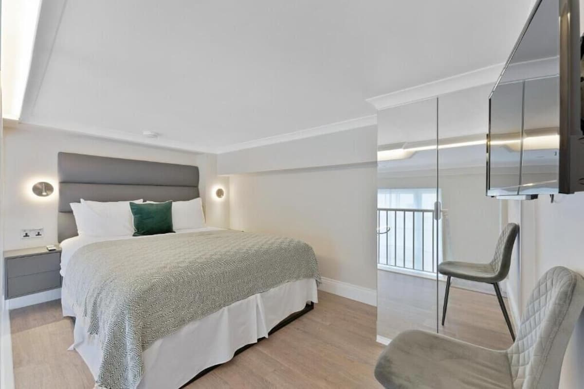 A modern bedroom with a bed, bedside tables, a chair, and a TV mounted on the wall.