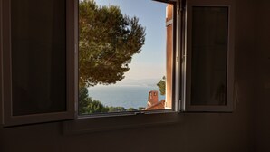 A window with a view of a tree and a distant building. - T2 vue mer 180° Avec balcon, Air-conditioned, direct access to the sea, Parking, Piscine (Saint-Cyr-sur-Mer)