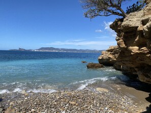 A rocky shoreline with clear blue water, pebbles, and a distant view of a town and mountains. - T2 vue mer 180° Avec balcon, Air-conditioned, direct access to the sea, Parking, Piscine (Saint-Cyr-sur-Mer)