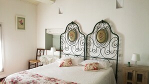 A bedroom with a bed, two decorative headboards, a wooden nightstand, a chair, and a small table with a lamp. - Agriturismo Morattina (Brisighella)