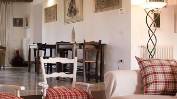 A cozy living room with a wooden ceiling, a dining table with chairs, and a sofa with plaid cushions. - Agriturismo Morattina (Brisighella)