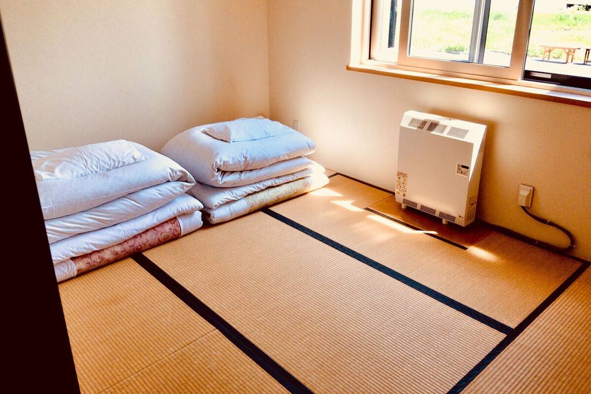 A room with tatami mats, a heater, and neatly stacked bedding.