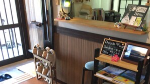 Interior de uma cafeteria com balcão de madeira, um sapateiro e uma vitrine de caixa.