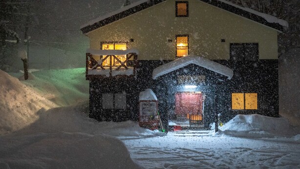 Uma casa coberta de neve, com entrada iluminada e porta da garagem visível.